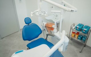 A clean and modern dental clinic featuring a blue dental chair, equipment, and sterile supplies.